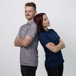 A grey and a navy blue women's polo shirt, both featuring logos, worn by two models standing back-to-back.