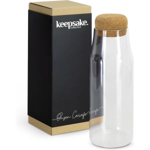 A clear glass carafe with a cork lid, presented beside its black and gold packaging.