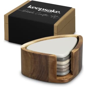 A wooden holder containing four grey pebble coasters, placed beside a black box with branding.