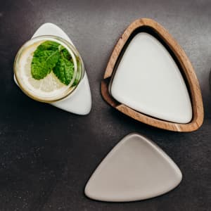 A set of three pebble-shaped coasters in white, grey, and wood, with a drink bottle beside them.
