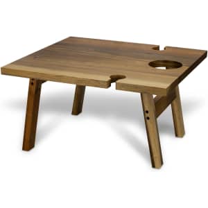 A square wooden folding table with a natural finish, featuring a hole for a drink, set on sturdy legs.