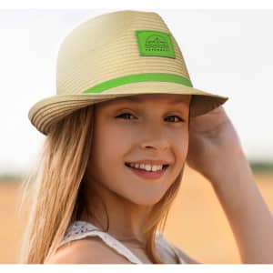 A straw fedora hat in beige with a green band and logo, worn by a smiling young girl outdoors.