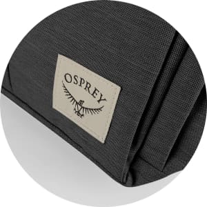 A close-up of a dark grey backpack fabric featuring an Osprey logo patch on the side.