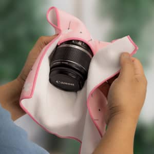 A hands holding a pink and white patterned cloth with a black camera lens partially wrapped inside.