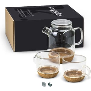 A glass tea pot with a handle and two matching transparent cups, featuring cork bases, presented in a box with branding.