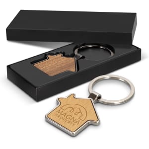 A house-shaped key ring in silver and wood, presented in a stylish black box. The key ring features a logo.