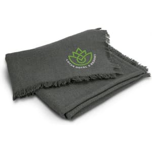 A green throw blanket with a fringed edge and a logo in the corner.