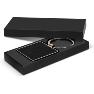 A square black key ring with a textured surface, presented in a sleek black gift box.
