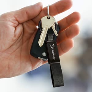 A hand holding a black key fob with two silver keys attached and a black key ring featuring a logo.