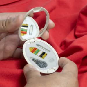 A compact sewing kit with a mirror, featuring colourful threads, needles, and safety pins, held against a red background.