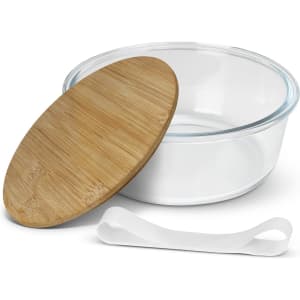 A glass food container with a wooden lid and a white elastic band. The container is clear and round.