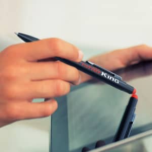 A stylus pen with a black body and a red tip, featuring a textured grip and a logo on the barrel.