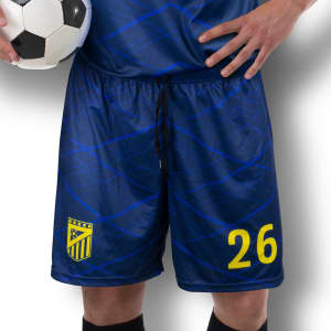 Custom men's soccer shorts in navy blue with a pattern, featuring a yellow number and logo. A soccer ball is held.