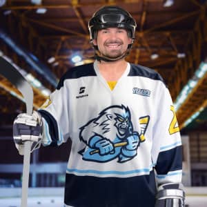 A hockey player in a white and navy custom jersey featuring a graphic design, holding a hockey stick, and wearing a helmet.