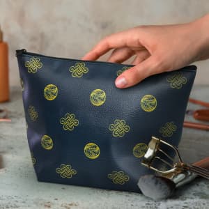 A medium navy cosmetic bag with gold patterns, featuring a hand reaching for it, alongside makeup brushes.