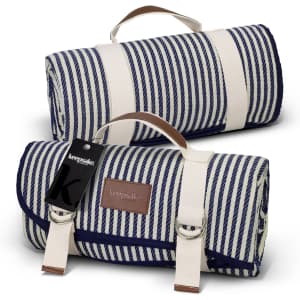 A blue and white striped picnic blanket rolled up, featuring a carrying handle and a logo tag.