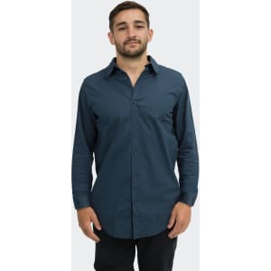 A man stands wearing a navy blue button-up shirt with long sleeves, featuring a collar and a logo.