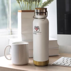 A drink bottle in white with a bamboo base, featuring a logo. A white mug and keyboard are in the background.