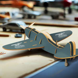 A wooden model aircraft in grey, featuring intricate details and a logo, displayed on a workspace with tools.