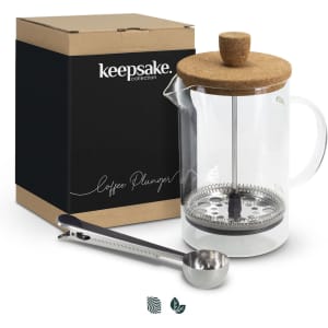 A coffee plunger with a glass body, cork lid, metal filter, and a matching coffee scoop in a boxed package.