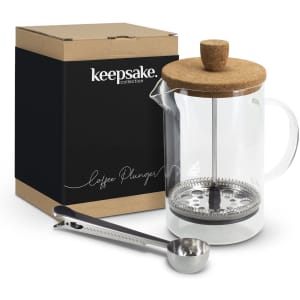 A glass coffee plunger with a cork lid, accompanied by a stainless steel measuring spoon, in a box with branding.