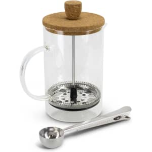 A clear glass coffee plunger with a cork lid, a stainless steel base, and a measuring spoon.
