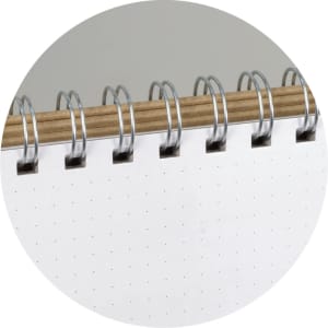 A white notepad with a spiral binding, featuring dotted pages and a wooden cover.