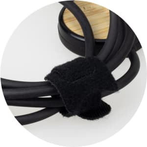 A black charging cable with a fabric tie, coiled neatly around a bamboo base, featuring a logo.