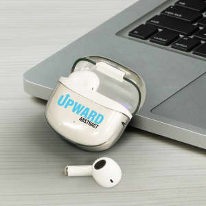 A pair of white Bluetooth earbuds in a charging case, placed next to a laptop on a grey surface.