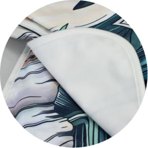A blanket featuring vibrant colours and intricate patterns, with a soft white underside. It has branding visible.