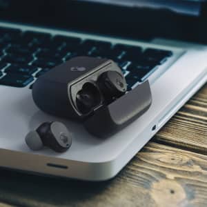 A pair of black Skullcandy Mod TWS earbuds and their charging case on a laptop keyboard.