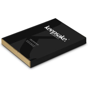 A black rectangular box with a gold inside, featuring a logo and design for the Keepsake Pebble Serving Board.