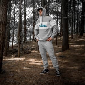 A unisex hoodie in grey with a logo, displayed on a person standing amidst trees in a forest setting.