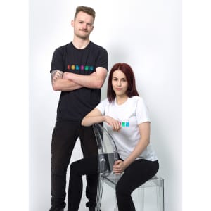 A black men's t-shirt and a white women's t-shirt with a logo are displayed on models against a plain background.
