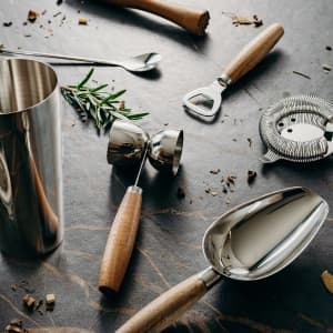 A cocktail shaker, jigger, spoon, strainer, and a bottle opener with wooden handles and stainless steel elements.