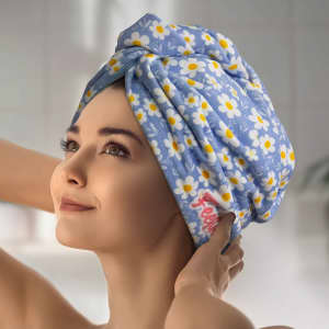 A woman wearing a light blue hair towel decorated with white daisies and yellow accents, featuring a logo.