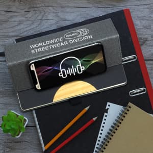 A grey Atoll Notebook with a phone and graphic design on top, alongside a small plant and various stationery items.