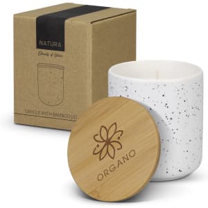A speckled white candle in a jar with a bamboo lid, displayed alongside its brown cardboard packaging.