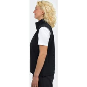 A woman stands sideways wearing a black vest with a high collar. The vest is sleeveless and fitted.
