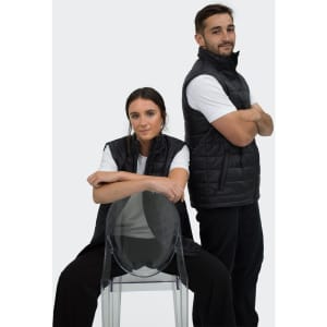 Black puffer vest worn by two models, one seated and one standing, both in white t-shirts and casual pants.