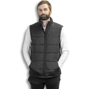 A man in a dark grey puffer vest stands with hands in pockets against a white background, featuring a logo on the vest.