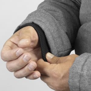 A grey puffer jacket sleeve is shown, with a close-up of a hand adjusting the cuff. The jacket features a logo.