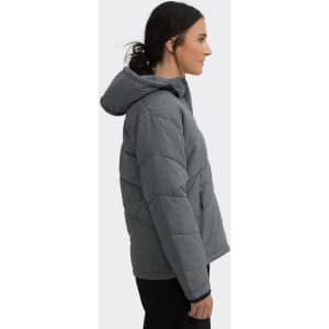 A woman is wearing a grey puffer jacket with a hood, showcasing a side profile view. The jacket features stitched detailing.