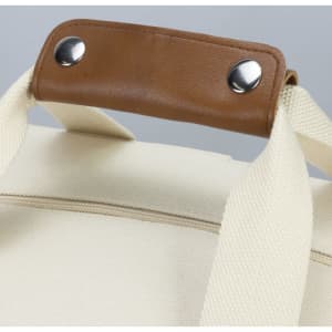 A cream cooler tote bag with a sturdy brown handle and silver studs, featuring a fabric exterior.