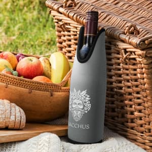 A drink bottle cooler in grey features a logo and is positioned next to a woven basket filled with fruits.
