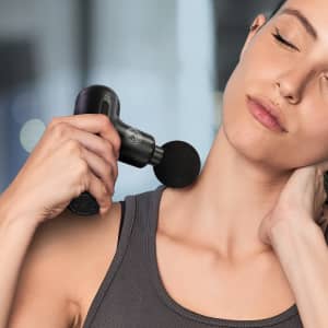 A black handheld massager is being used on a woman's neck, with a lightly blurred background.