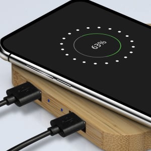 A bamboo wireless charging hub with a smartphone displaying charging status. The hub has two connected cables.