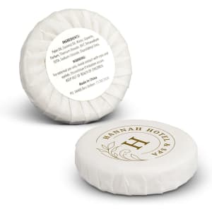 A round, white travel soap with a decorative logo and packaging, featuring a floral design.