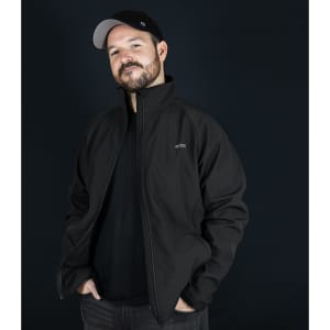 A man wearing a black Swiss Peak Urban Softshell Jacket with a logo, against a dark background.