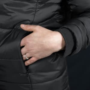 A close-up of a hand resting on a zip pocket of a black puffer jacket with ribbed cuffs.